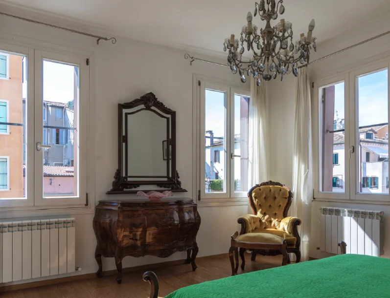Camera da letto luminosa con arredi d'epoca, poltrona in velluto e vista panoramica nell'appartamento Bastianello Grand Canal a Chioggia.