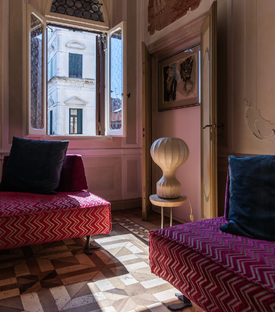 Scorcio del salotto di Suite Attilia a Chioggia, con finestra storica aperta su un palazzo d'epoca, poltrone di design e pavimento in legno intarsiato.